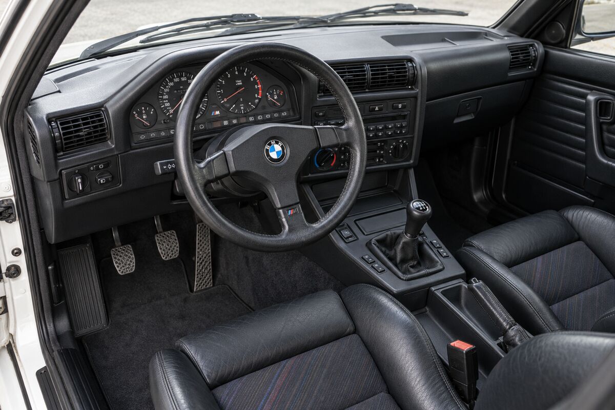 The cabin of a first-generation BMW M3, with its three-spoke M steering wheel and M-stripe seats.